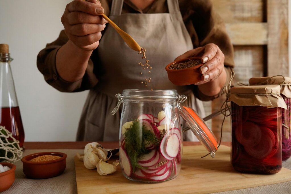 pexels-photo-28645474-28645474 Close-up of hands preparing homemade pickles with spices in a rustic kitchen setting.