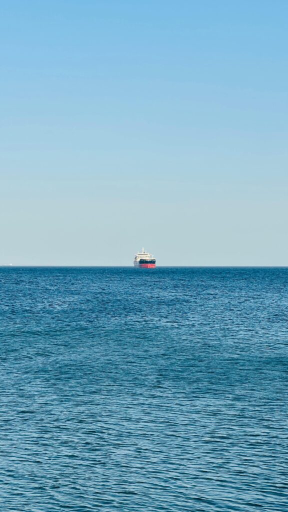 pexels-photo-32104238-32104238 Cargo ship sailing alone on the clear blue ocean under a bright sky.